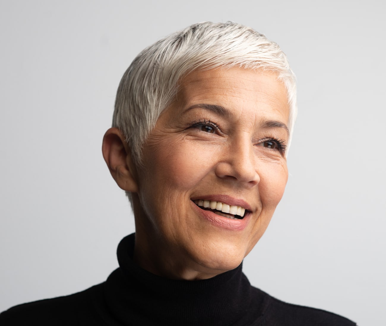 An Older Woman With Short, White Hair Smiling And Looking Off To The Right