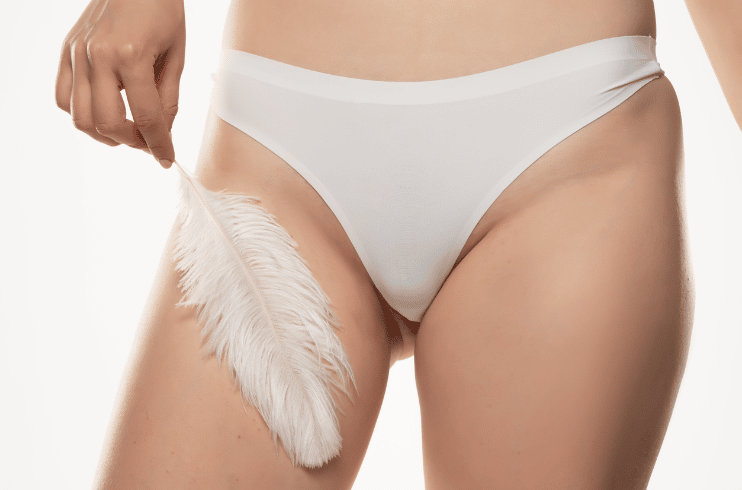 A Woman Poses In White Underwear While Holding A Feather Against Her Thigh