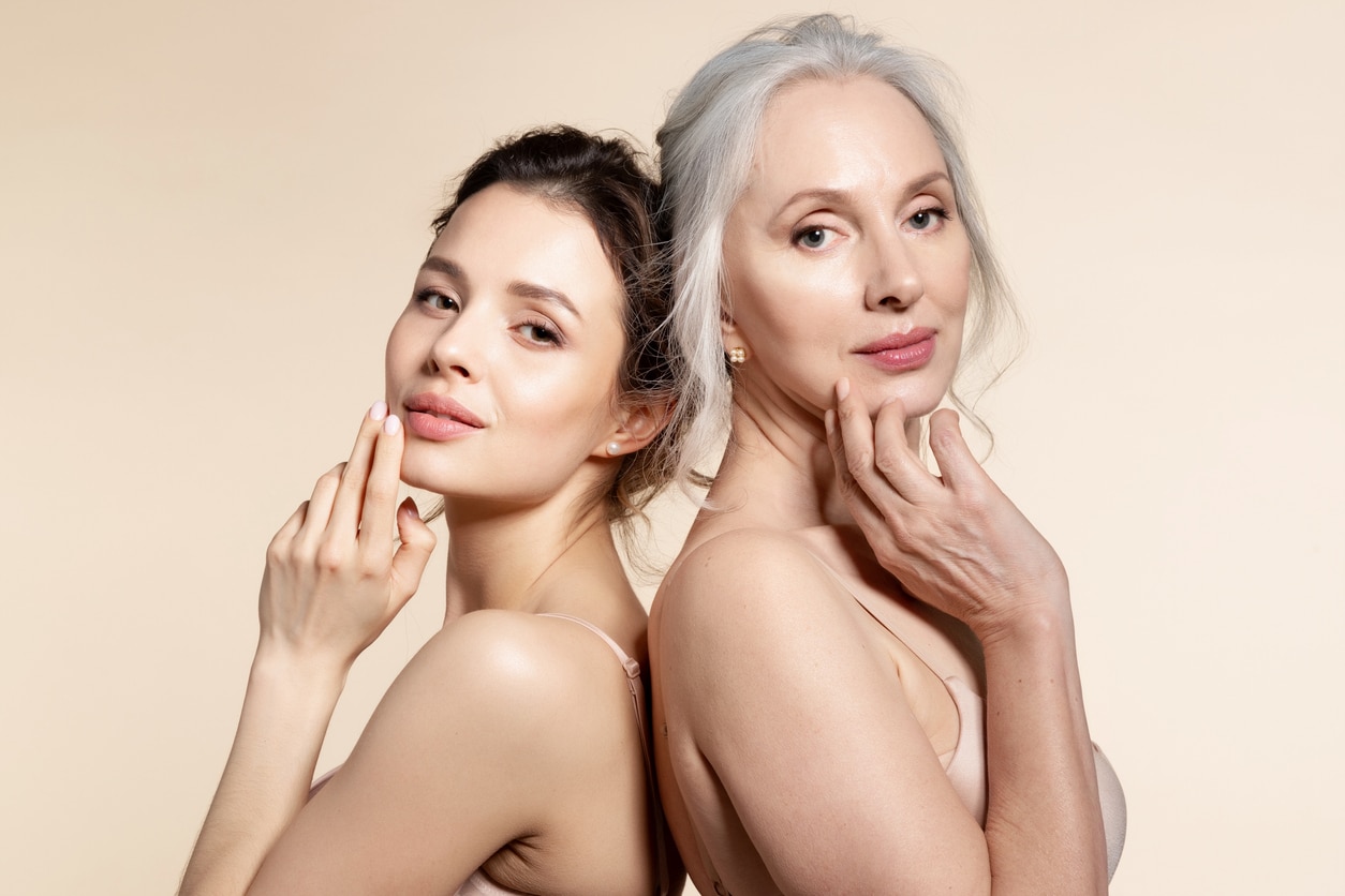 A Brunette Woman And Older Woman With Their Hands On Their Faces With No Fine Lines Or Wrinkles.